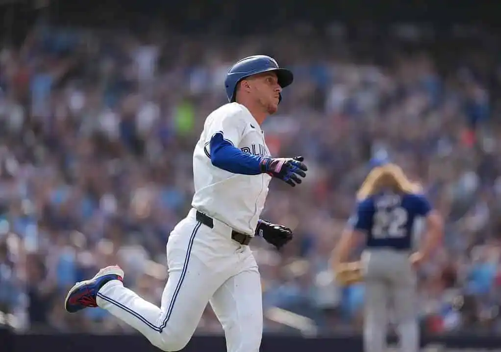 Toronto Blue Jays player runs the bases after making contact, with the crowd cheering in the background during an MLB game.