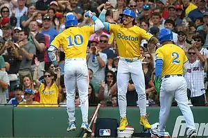 Boston Red Sox players in bright yellow City Connect uniforms celebrate a big play with high-fives as fans cheer in the background.