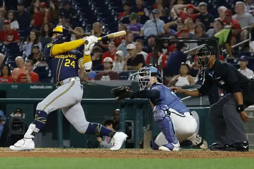 A baseball player swings his bat high above home plate, while a catcher crouches low, ready to receive the pitch in a lively stadium.