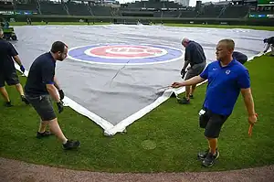 Grounds crew covers Wrigley Field with a large tarp featuring the Chicago Cubs logo.