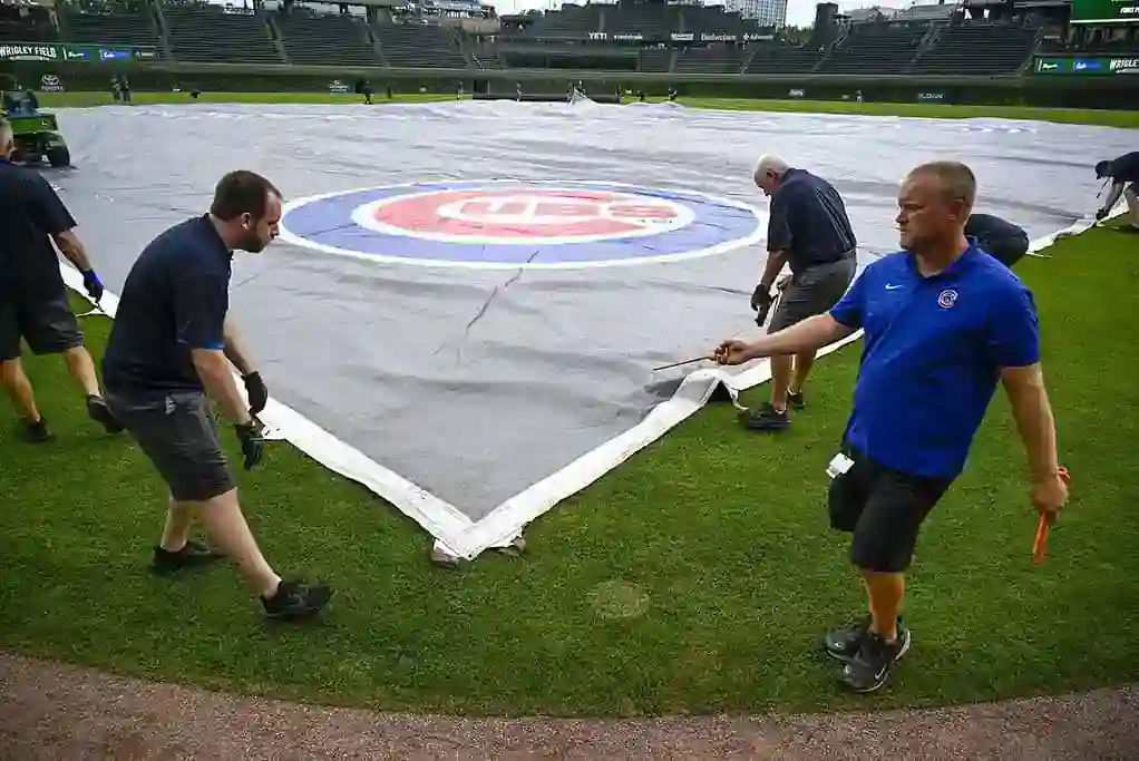 Grounds crew covers Wrigley Field with a large tarp featuring the Chicago Cubs logo.