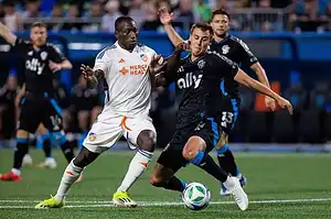 A tense moment in a soccer match is captured, showing two players intensely vying for possession of the ball.