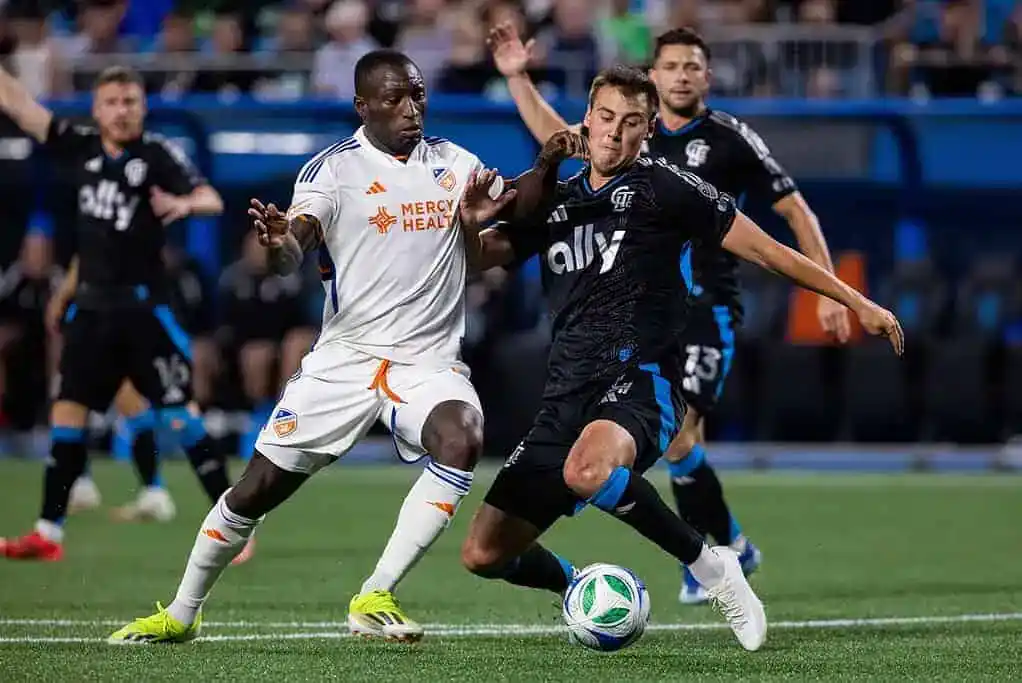 A tense moment in a soccer match is captured, showing two players intensely vying for possession of the ball.