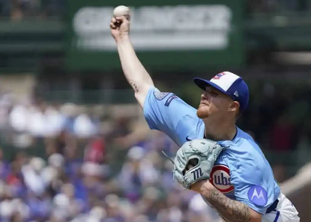 A pitcher in a light blue Chicago Cubs jersey winds up to throw a baseball in a stadium filled with fans.