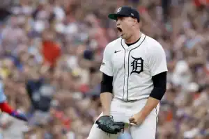 A Detroit Tigers player in a white jersey celebrates triumphantly on the pitch, surrounded by a cheering crowd.