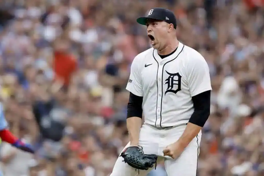 A Detroit Tigers player in a white jersey celebrates triumphantly on the pitch, surrounded by a cheering crowd.