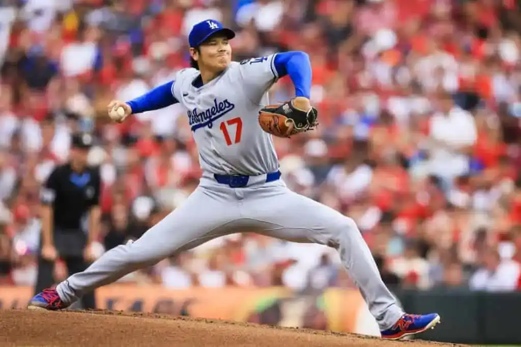A baseball pitcher in a gray Los Angeles Dodgers uniform prepares to throw, surrounded by a cheering crowd in a stadium.