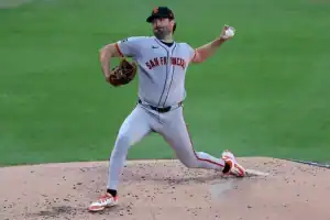 A baseball pitcher in a gray San Francisco jersey winds up to throw a pitch, with motion captured on the mound surrounded by dirt.