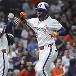 Two baseball players in Astros uniforms celebrate a successful play, one giving a fist bump while holding a bat. Crowd in the background.