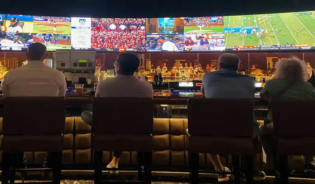 Personas viendo pantallas deportivas en un bar, representando la relación entre inteligencia artificial y apuestas deportivas.