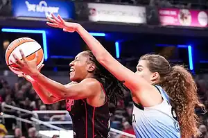 A basketball player in a red jersey attempts a layup while being closely defended by another player in a blue and white uniform.