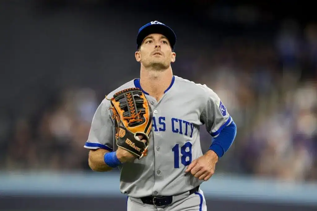A baseball player in a gray jersey with the text "Kansas City" is running on the field, wearing a glove on his left hand.