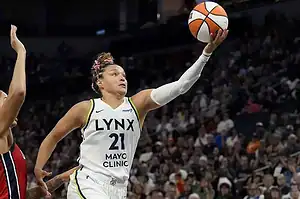 A basketball player in a Lynx jersey passes the ball in a packed arena, showcasing athleticism and teamwork during a game.