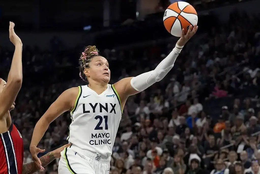 A basketball player in a Lynx jersey passes the ball in a packed arena, showcasing athleticism and teamwork during a game.