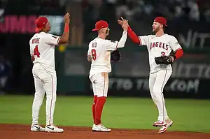 Three baseball players in white and red uniforms from the Angels celebrate together on the field, sharing high fives and camaraderie.