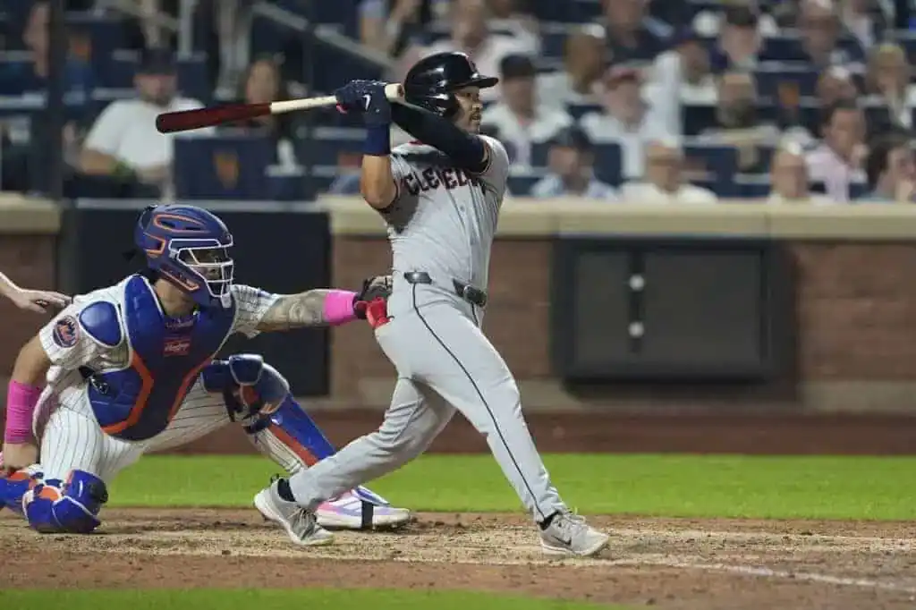 A baseball player in gray swings a bat, while the catcher in blue gear prepares to catch a pitch during a night game.