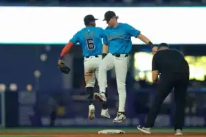 Two Miami Marlins baseball players celebrate a play as an umpire approaches them at a baseball stadium.