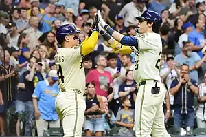 Two baseball players celebrate a successful play with high fives, as an excited crowd cheers in the background.
