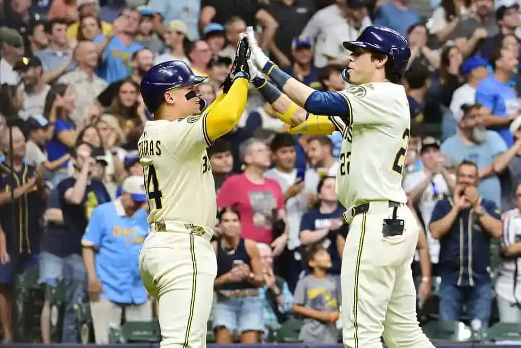Two baseball players celebrate a successful play with high fives, as an excited crowd cheers in the background.