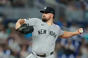 A New York Yankees pitcher in a gray uniform winds up to throw a baseball during a night game, focused on the pitch.
