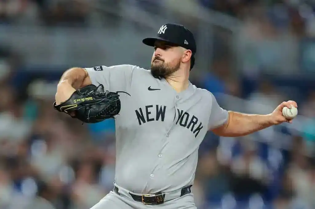 A New York Yankees pitcher in a gray uniform winds up to throw a baseball during a night game, focused on the pitch.