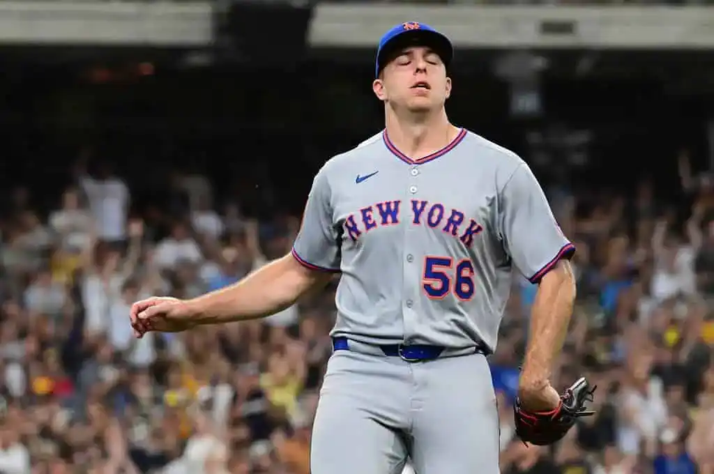 A New York baseball player in a gray jersey and cap stands on the field, celebrating amidst a cheering crowd.