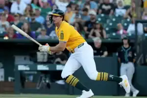 A player in a bright yellow baseball uniform swings a bat, focused intently on the game, with a crowd watching in the background.