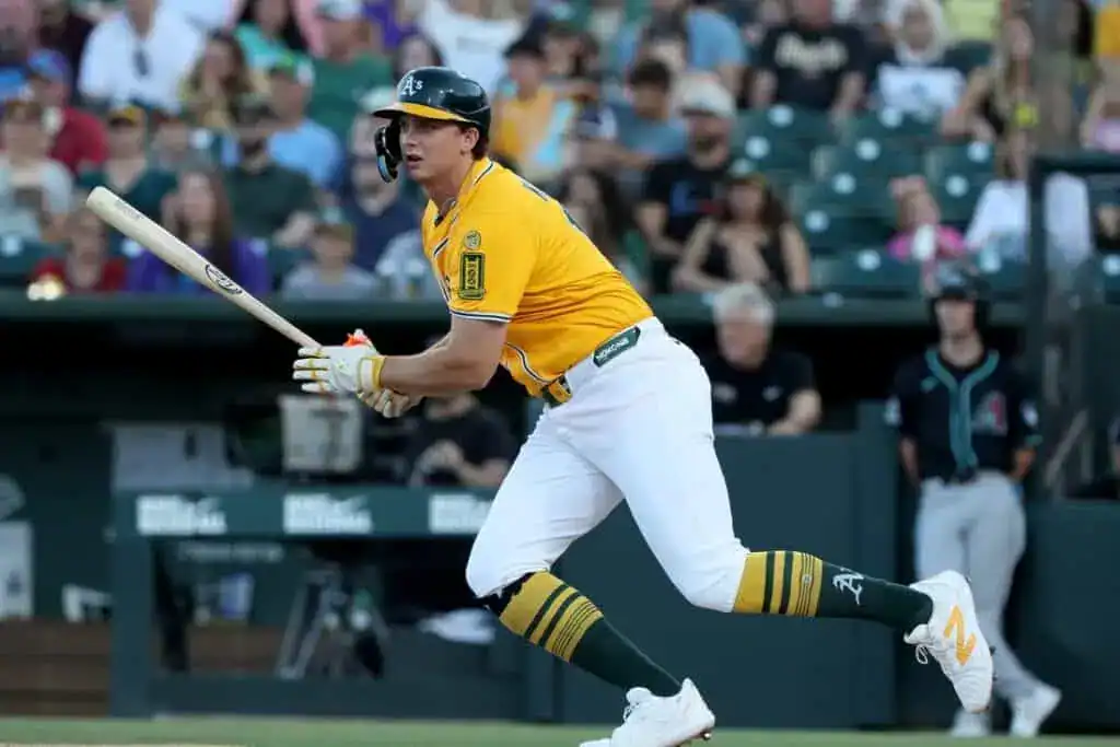 A player in a bright yellow baseball uniform swings a bat, focused intently on the game, with a crowd watching in the background.