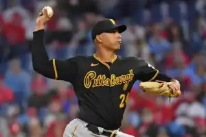 A Pittsburgh Pirates player in a black jersey prepares to throw a baseball, with the stadium and fans blurred in the background.