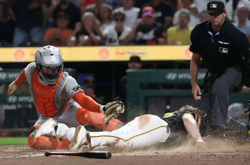 A baseball player slides into home plate as a catcher prepares to tag him, dust flying around them amid a tense game moment.