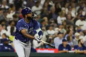 A baseball player in a dark blue uniform swings a bat as fans watch attentively in the background of a lively stadium.