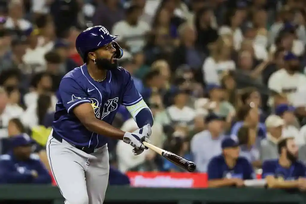 A baseball player in a dark blue uniform swings a bat as fans watch attentively in the background of a lively stadium.