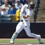 A baseball player, wearing a white uniform with navy blue accents, lunges hard to bat, his eyes focused on the ball.