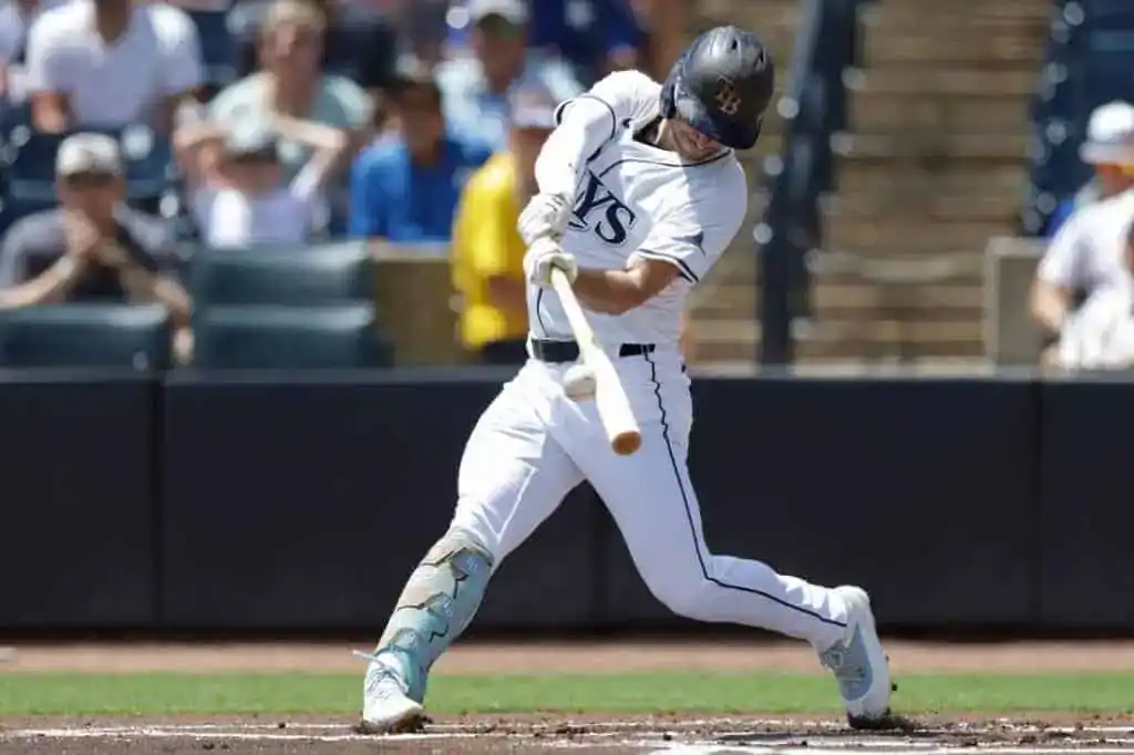 A baseball player, wearing a white uniform with navy blue accents, lunges hard to bat, his eyes focused on the ball.