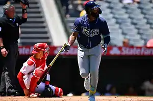 A baseball player from the Tampa Bay Rays runs toward first base, while a catcher in red crouches behind home plate.