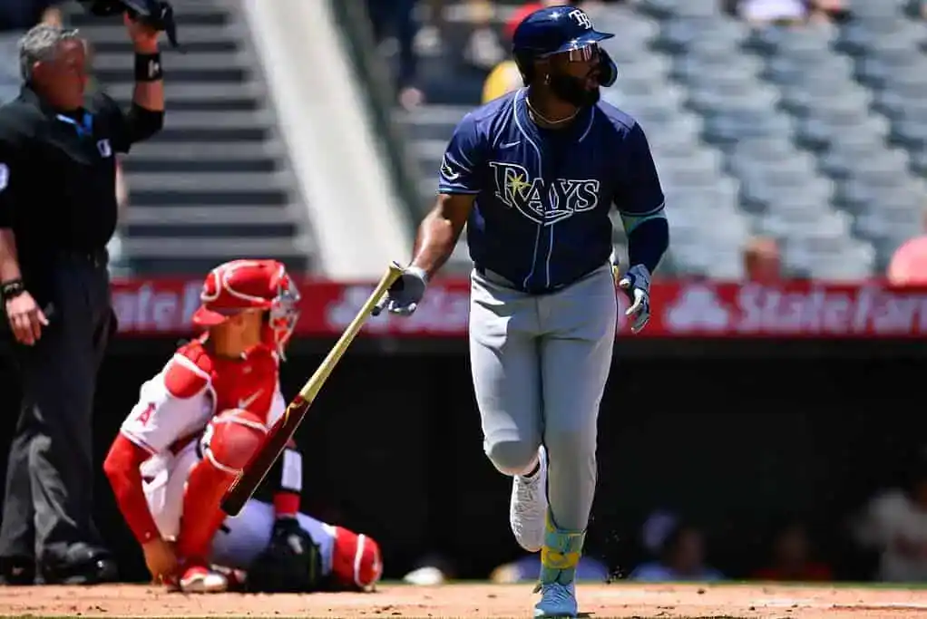 A baseball player from the Tampa Bay Rays runs toward first base, while a catcher in red crouches behind home plate.
