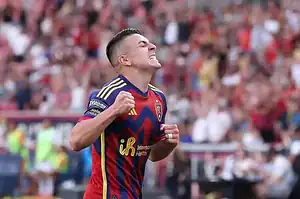 A soccer player, in the midst of a game, celebrates victoriously with a powerful expression of joy and triumph.
