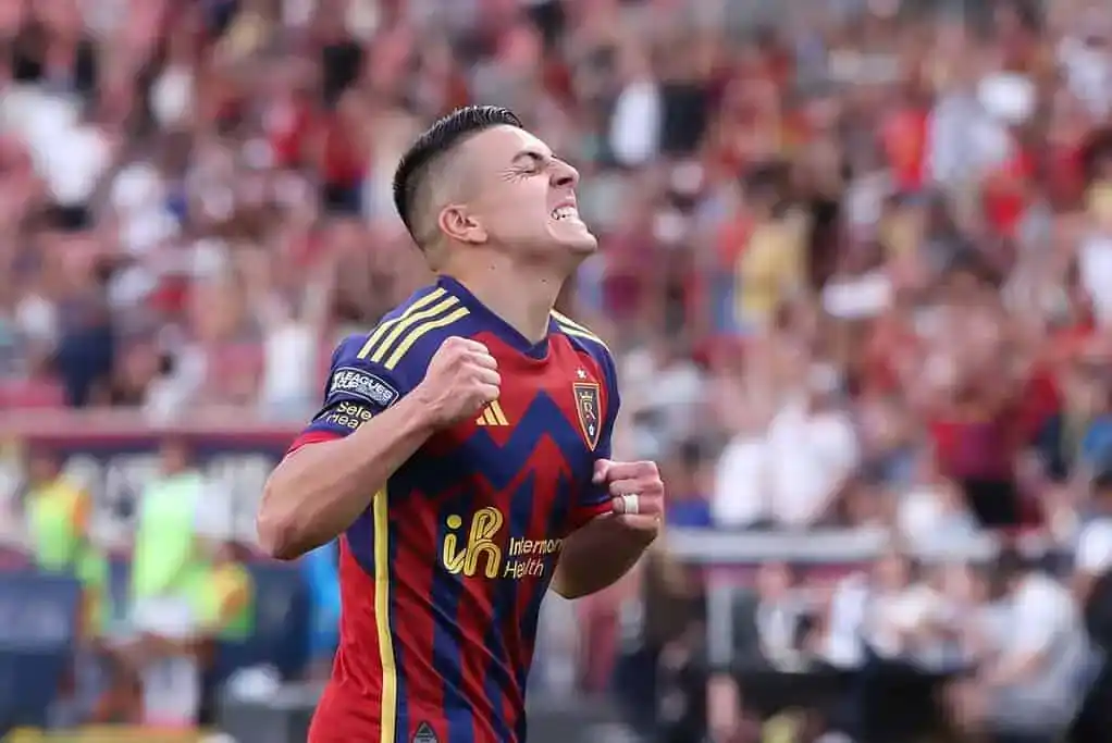 A soccer player, in the midst of a game, celebrates victoriously with a powerful expression of joy and triumph.