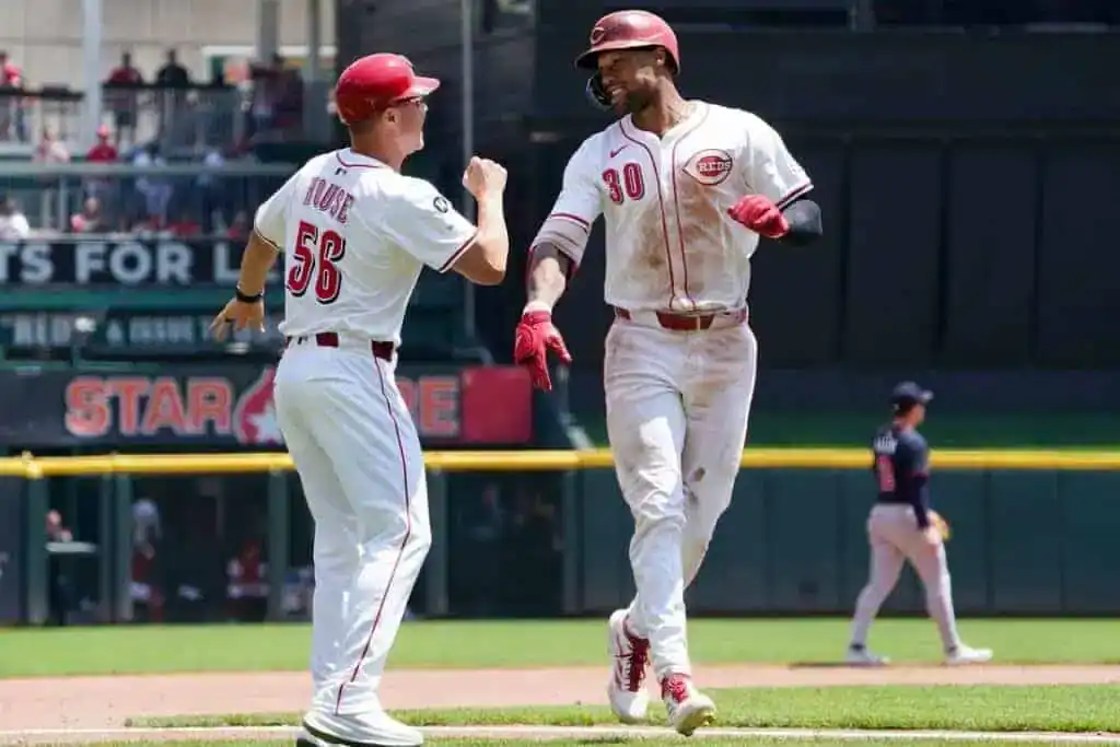Two baseball players celebrate in a sunny stadium, with one player in white uniform crossing home plate after a run.