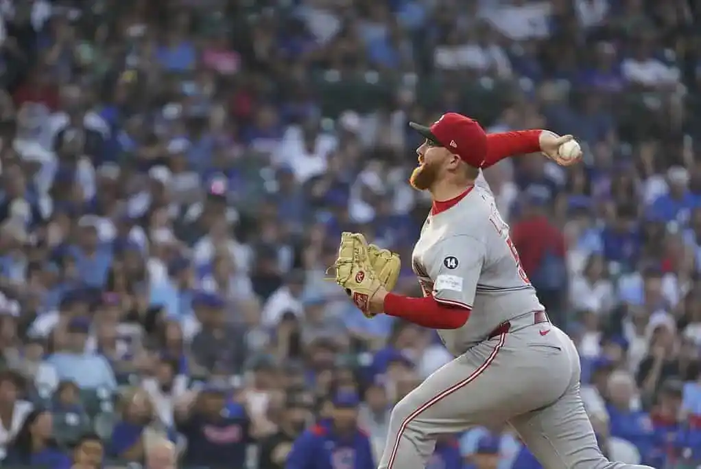 A pitcher in a gray uniform throws a baseball, surrounded by an audience at a baseball stadium.