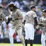 A group of baseball players in camouflaged team jerseys celebrates on the field during a game.