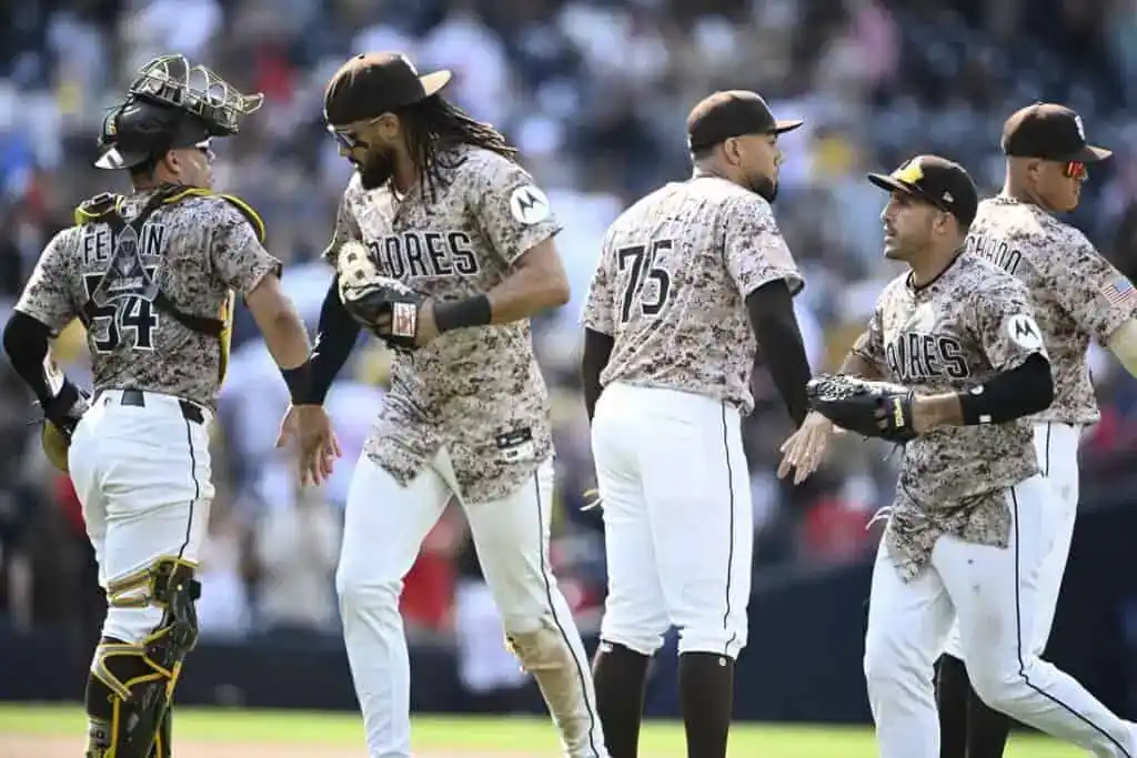 A group of baseball players in camouflaged team jerseys celebrates on the field during a game.