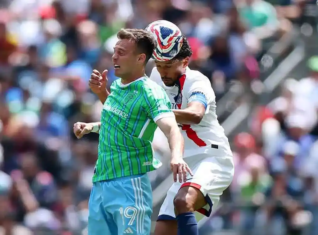 Two soccer players engage in a competitive moment on the field, surrounded by an energetic crowd in the background.