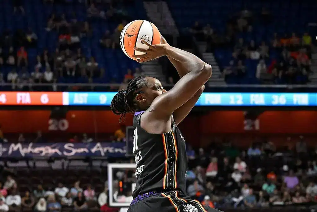 A WNBA player from the Phoenix Suns rises for a jump shot during a game against the Indiana Fever, with fans watching in the background.