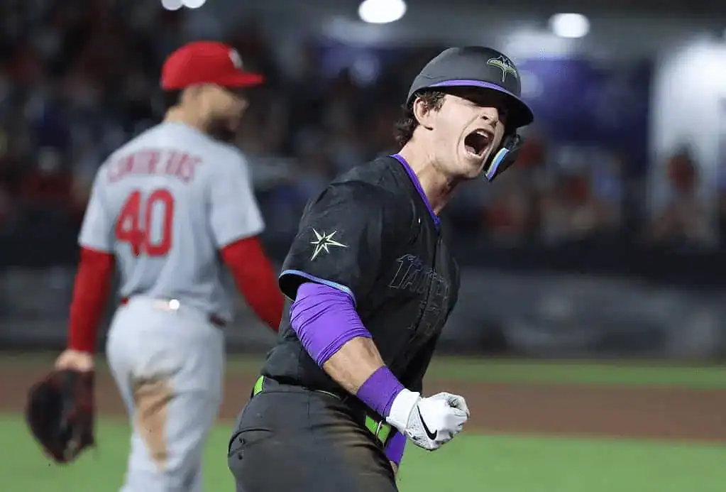Tampa Bay Rays player celebrating with a yell after a clutch play, while a St. Louis Cardinals pitcher walks in the background.
