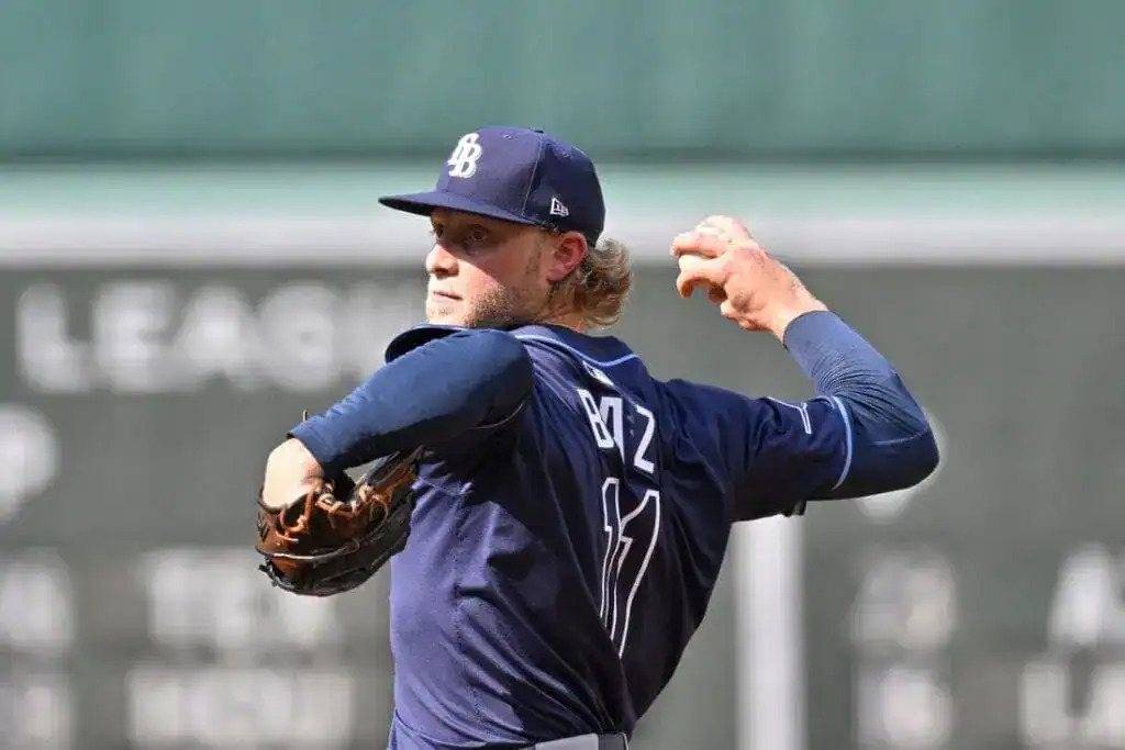 A baseball player in a blue jersey prepares to pitch, showcasing a focused stance and gripping a glove on the mound.