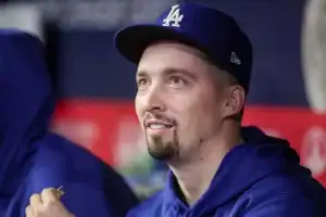 A young man wearing a blue Dodgers cap and hoodie sits in a dugout, appearing pensive while holding a small object.