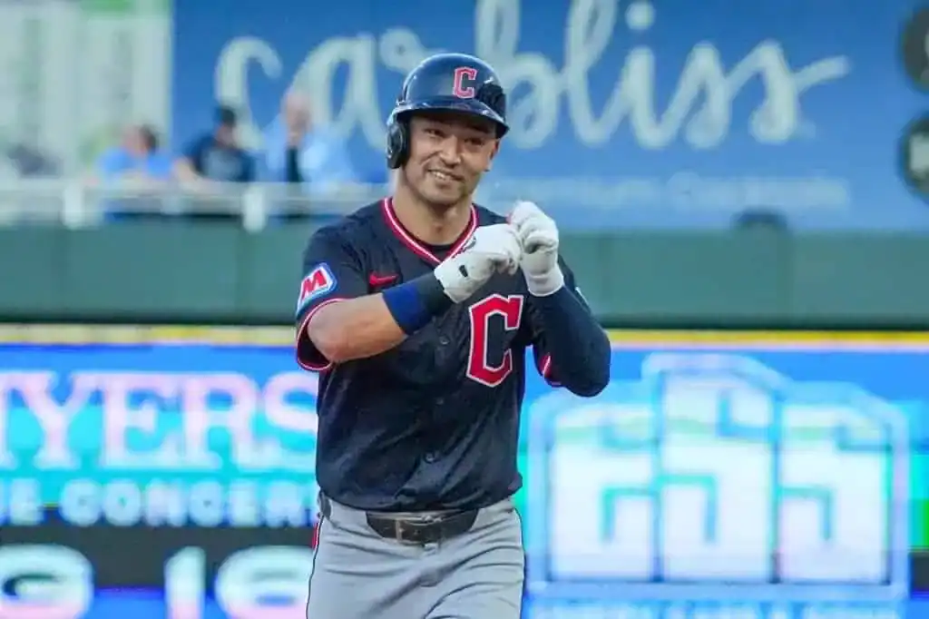 A baseball player in a black jersey with a red "C" celebrates on the field, with a colorful advertisement in the background.