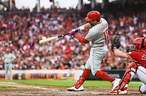 A baseball player swings at a pitch, with a catcher poised to receive the ball, amidst a crowd filled with enthusiastic fans.