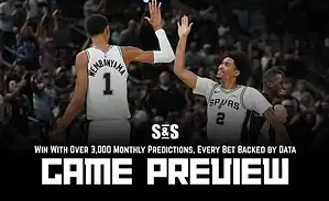 Two basketball players celebrate a play during a game, wearing San Antonio Spurs uniforms, with a crowd cheering in the background.